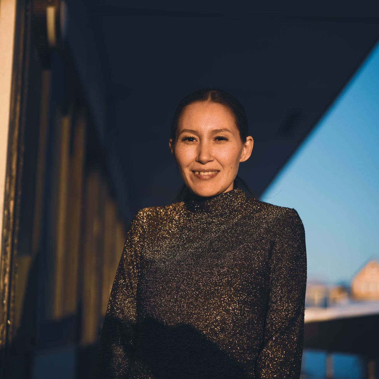A woman smiling warmly outdoors at sunset