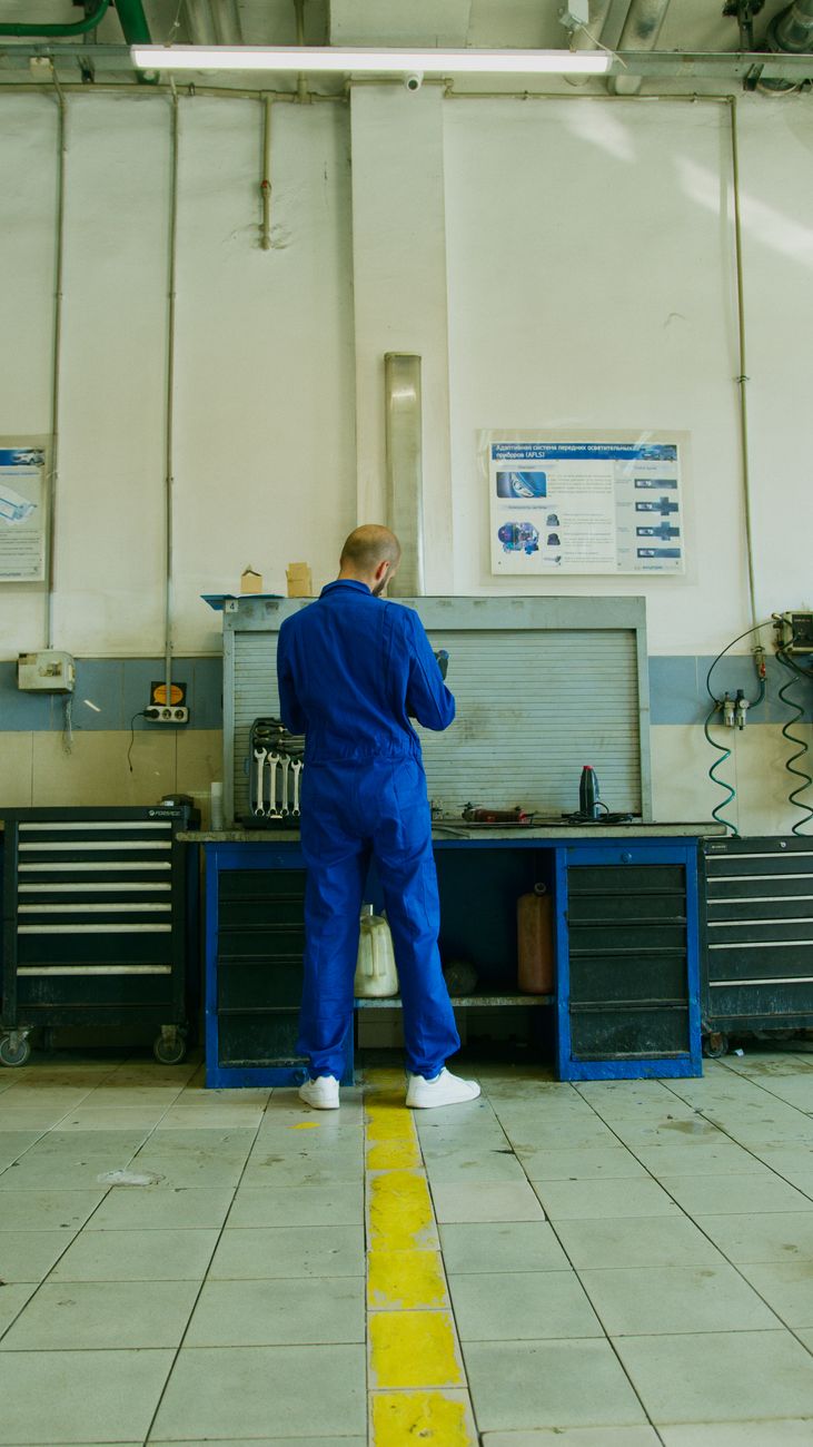 Mechanic in a blue coverall performing maintenance in a well-equipped workshop.